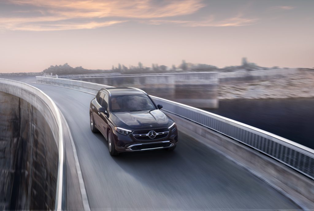 A 2026 Mercedes-Benz GLC driving along a curved elevated roadway at sunset with blurred scenery.