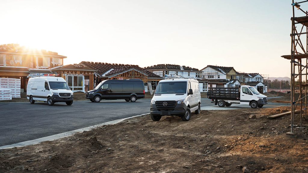 Several 2026 Mercedes-Benz Sprinter vans in different configurations parked at a new housing development under construction.