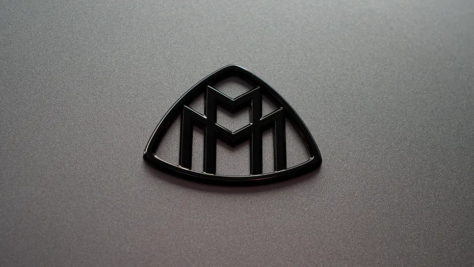 2027 Mercedes-Maybach S-Class Maybach emblem close-up on a dark exterior surface.