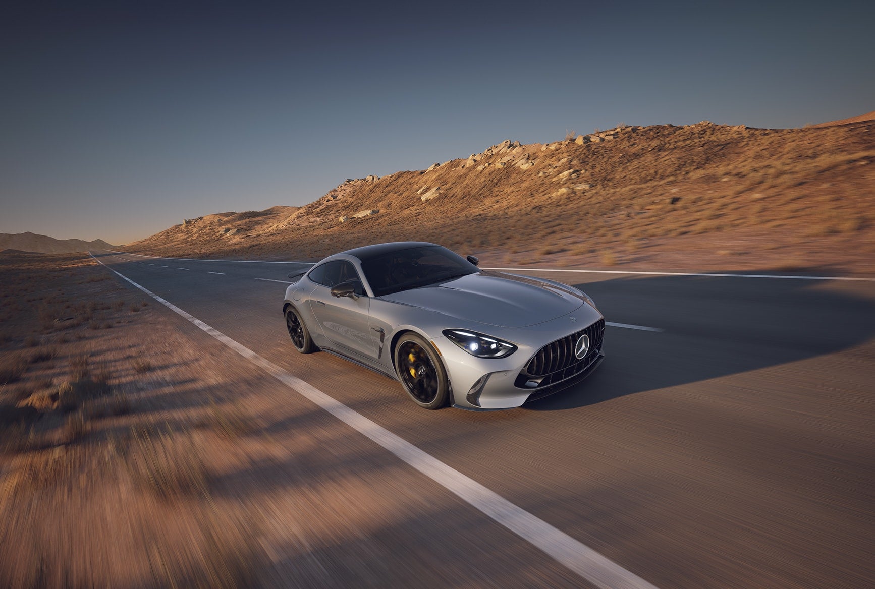 Silver 2027 Mercedes-Benz AMG GT 63 S E PERFORMANCE Coupe driving on a desert highway.