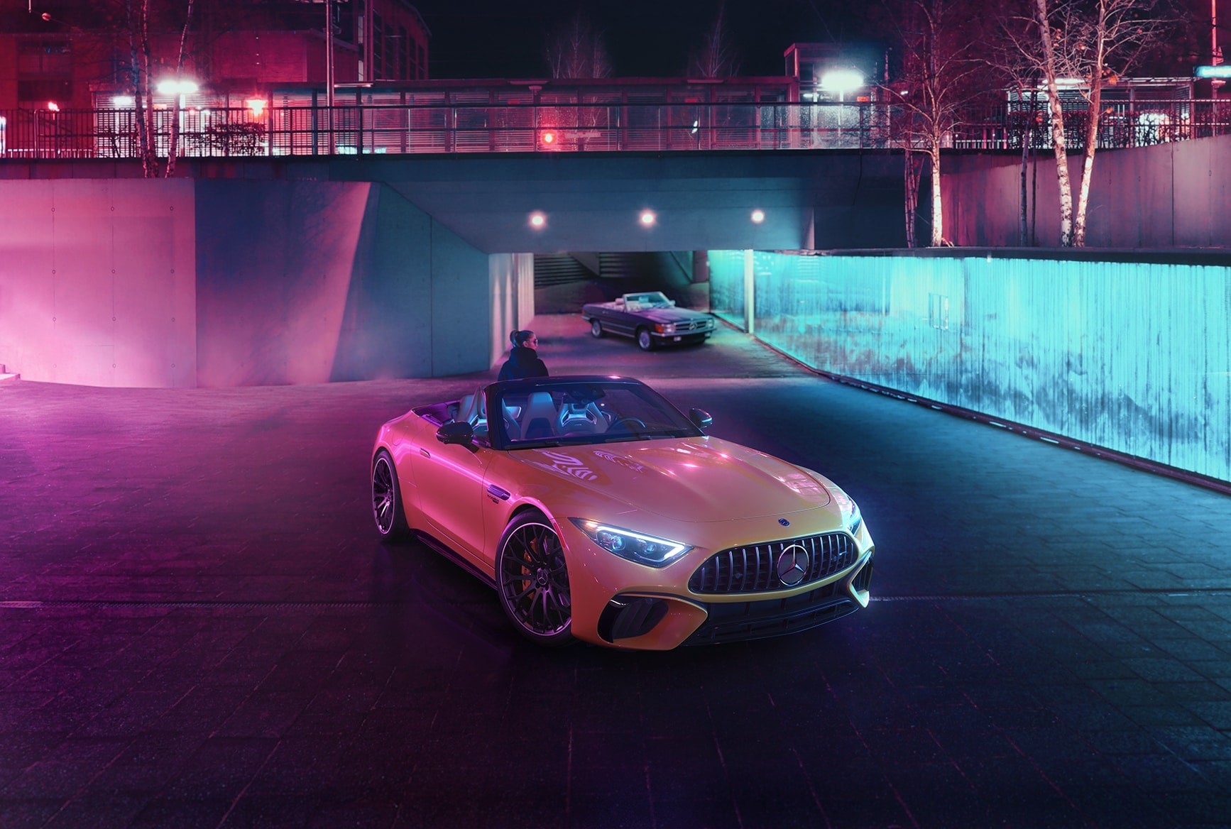 2027 Mercedes-Benz AMG SL 63 Roadster with its soft top lowered under colorful city lights.