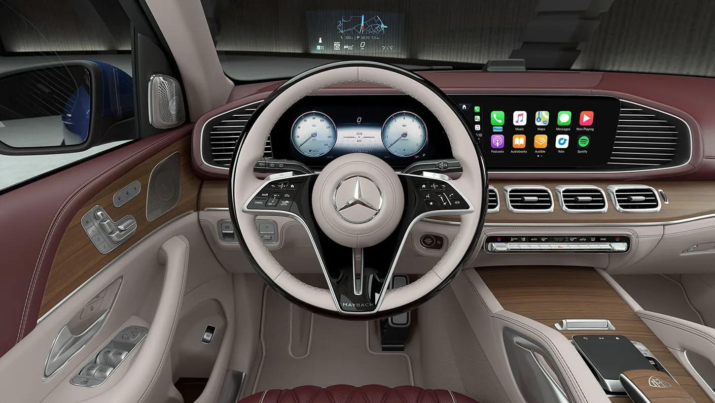 Mercedes-Maybach GLS front interior showing the steering wheel, digital displays, MBUX infotainment screen, wood trim, and leather dashboard