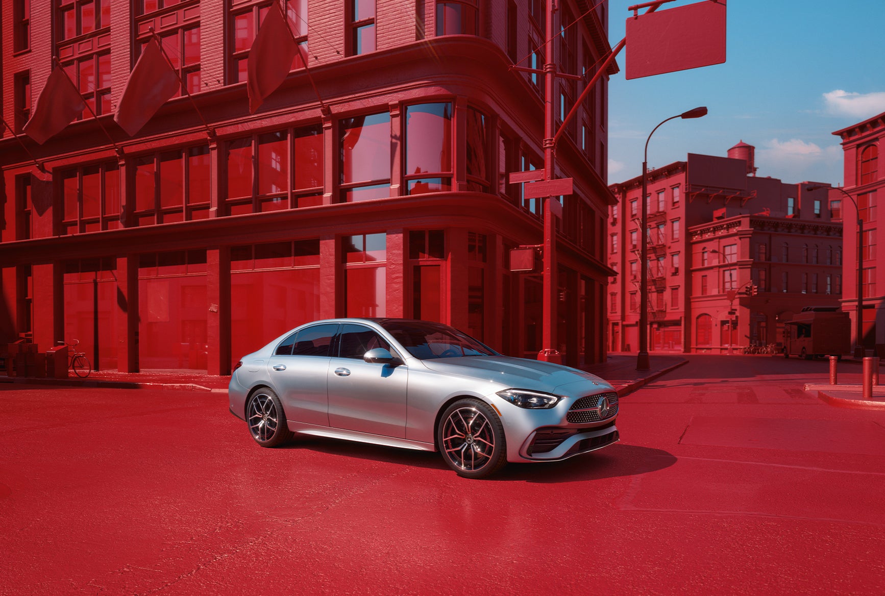 2027 Mercedes-Benz C-Class Sedan in silver parked on a city street with red architectural background.
