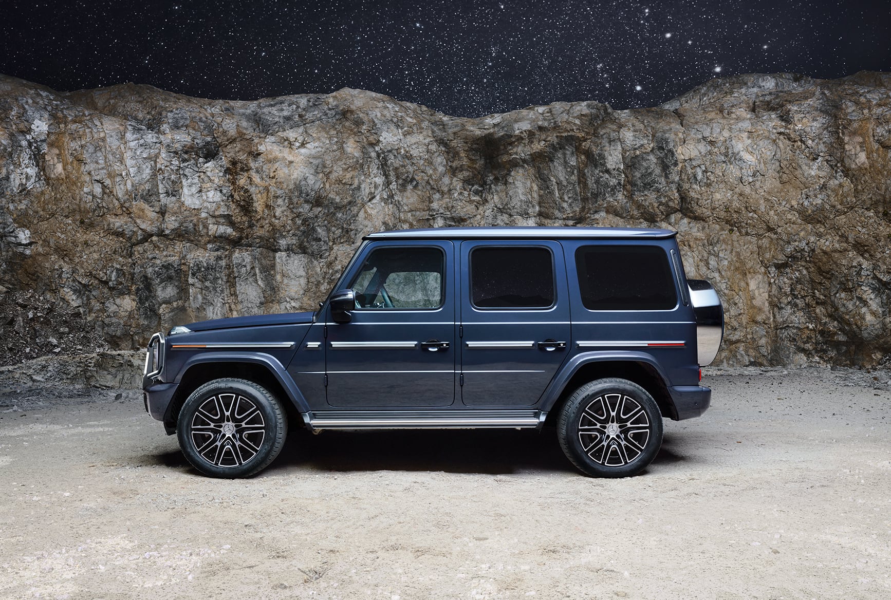 Mercedes-Benz G-Class luxury SUV side view parked outdoors with a rocky landscape in the background.
