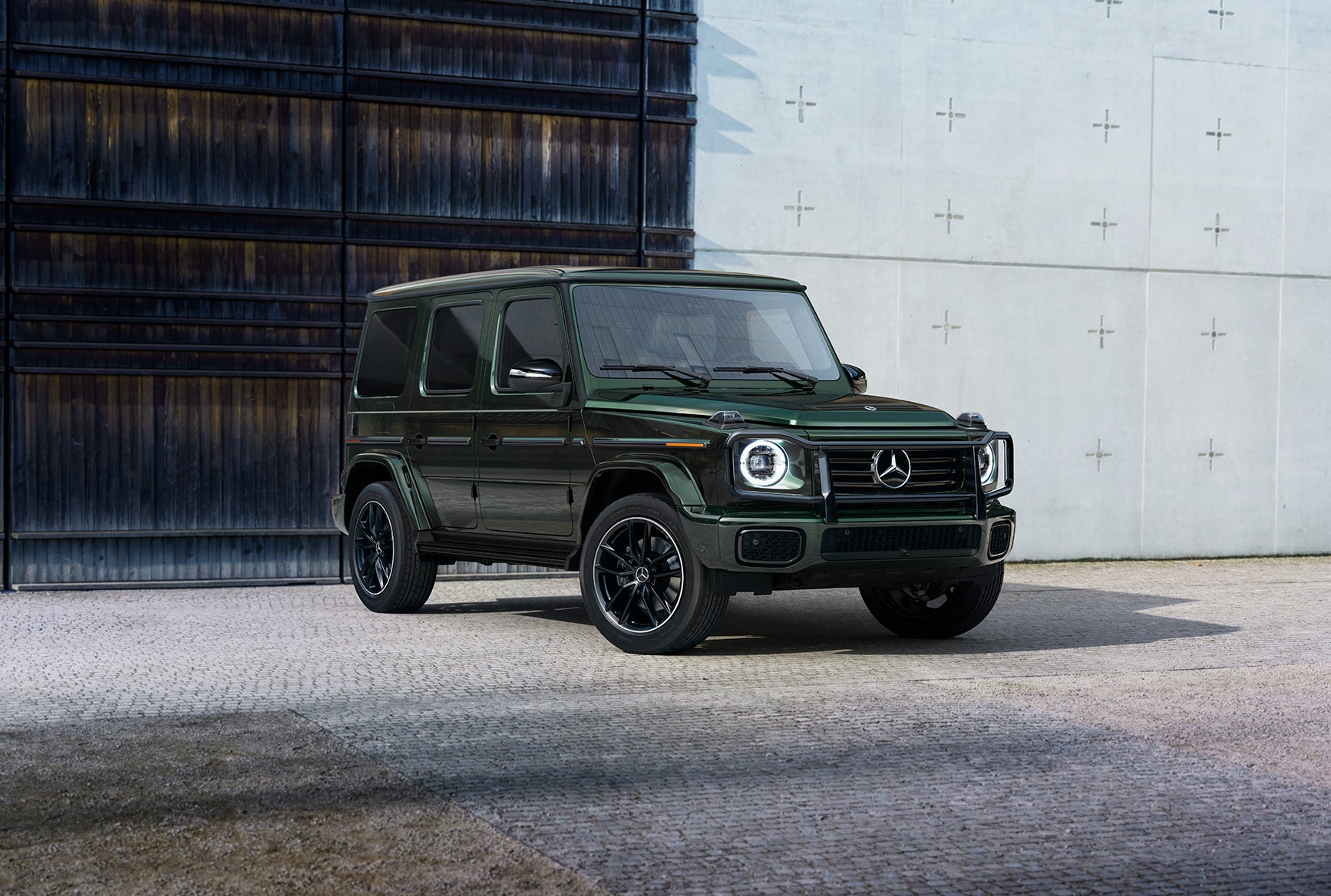 Mercedes-Benz G-Class luxury SUV with a dark green exterior parked in front of a modern industrial building.
