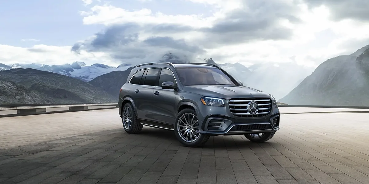 Gray Mercedes-Benz GLS shown from the front at a mountain overlook with dramatic clouds in the background